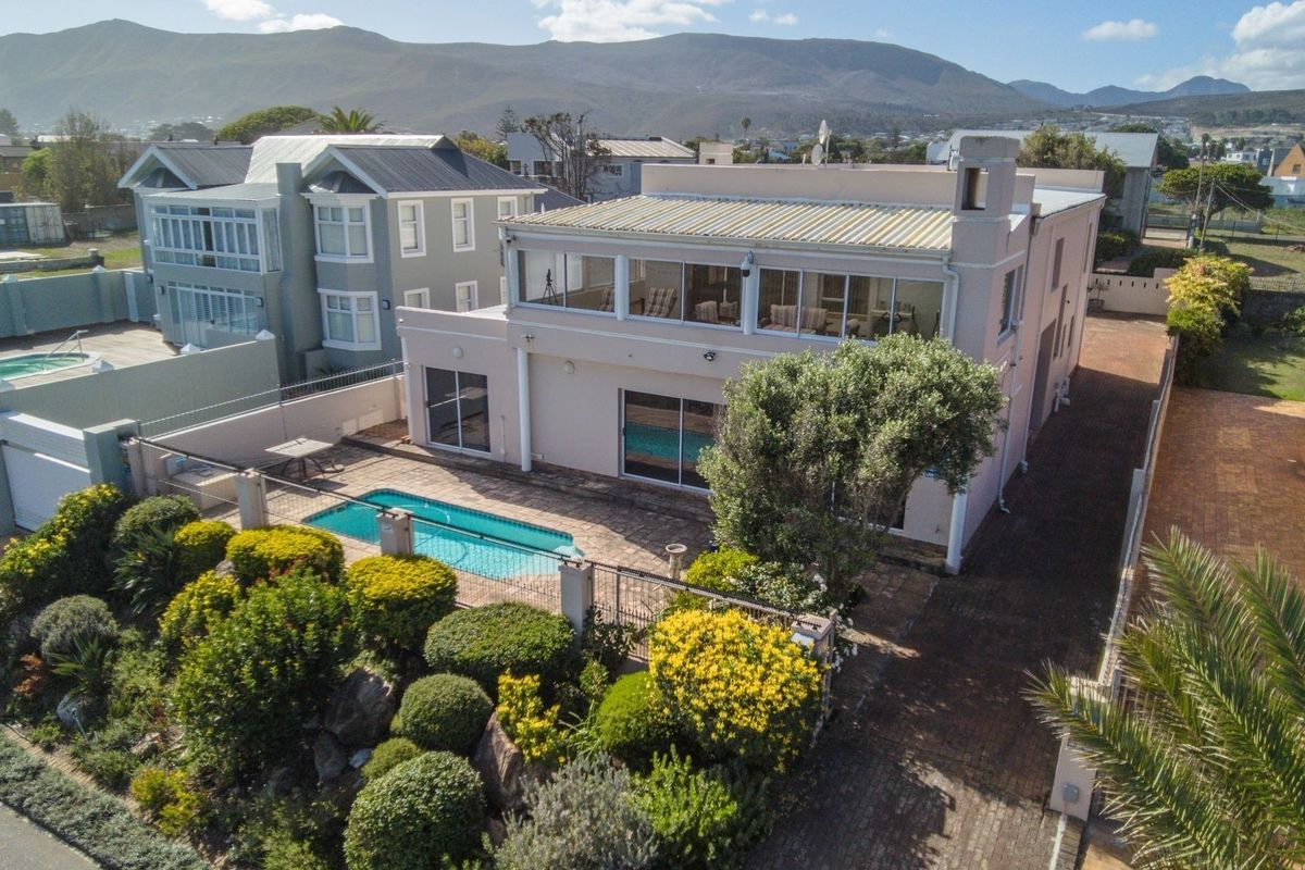 Aerial view of a multi-story residential property featuring a swimming pool, landscaped garden, paved driveway, and an upper-level balcony with mountain views.