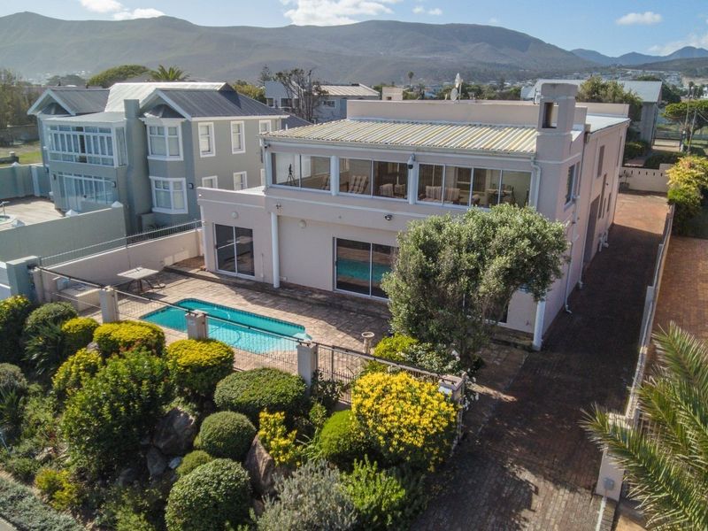 Aerial view of a multi-story residential property featuring a swimming pool, landscaped garden, paved driveway, and an upper-level balcony with mountain views.