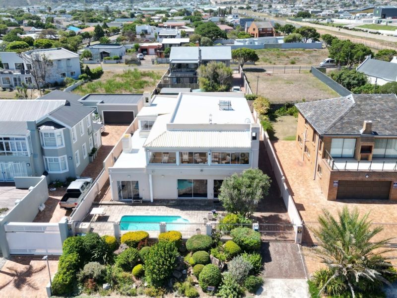 Aerial view of a residential property featuring a swimming pool, paved patio area, landscaped garden, and a flat-roofed house structure.