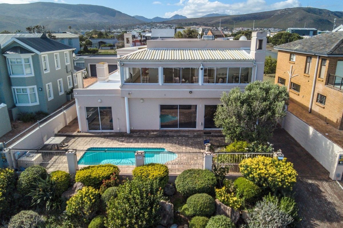 Aerial view of the rear exterior featuring a swimming pool, paved patio area, landscaped garden, and a two-story house with a balcony.
