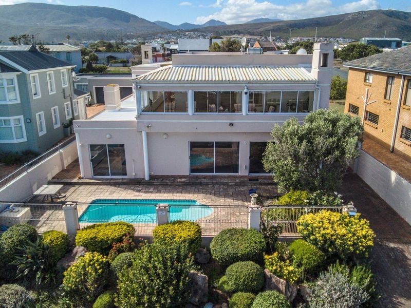 Aerial view of the rear exterior featuring a swimming pool, paved patio area, landscaped garden, and a two-story house with a balcony.