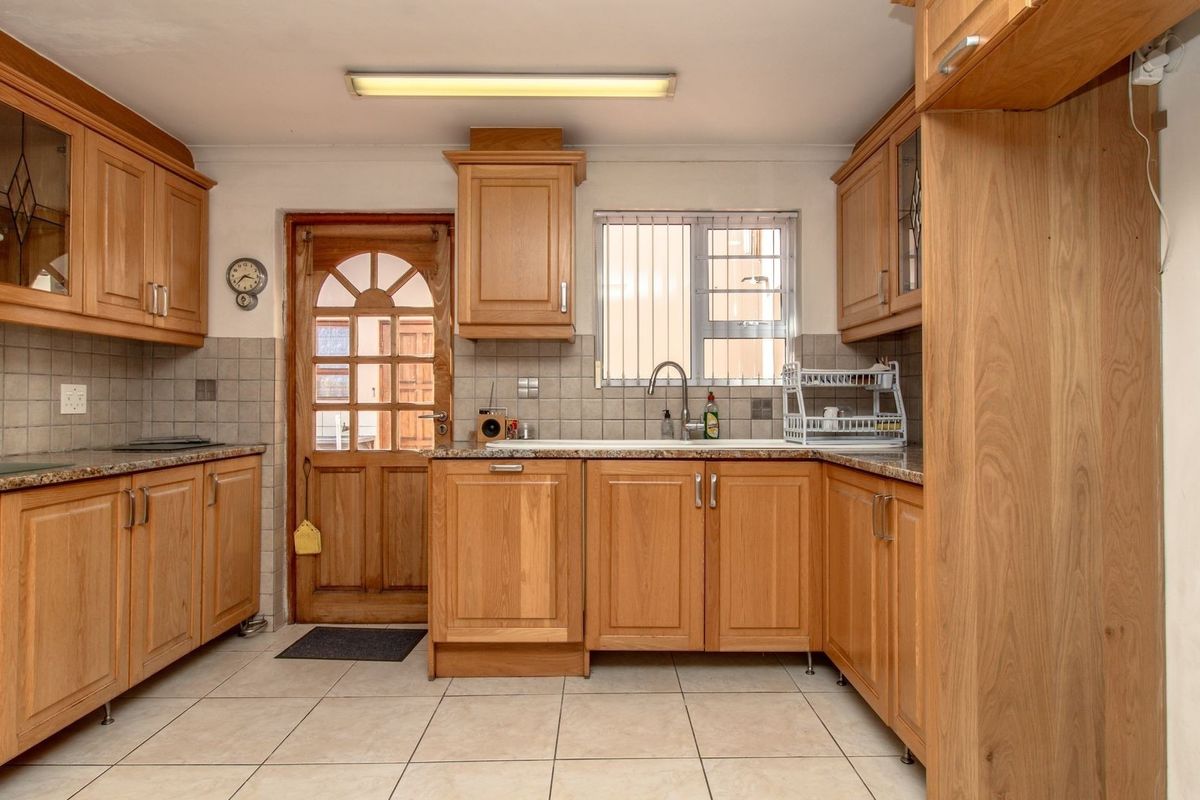 A functional kitchen featuring wooden cabinetry, granite countertops, tiled backsplash, and tiled flooring, with direct access to an exterior timber door.