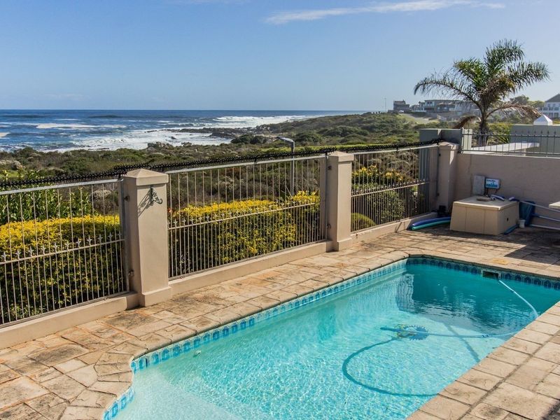 Outdoor pool area featuring stone paving, metal security fencing, and expansive ocean views.