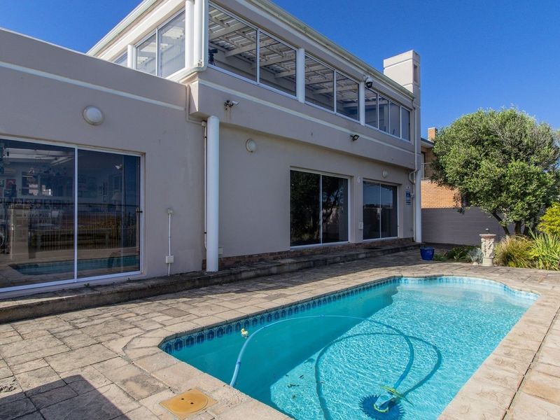 Rear exterior view featuring a swimming pool, paved patio area, and a two-story building facade with large sliding glass doors and an enclosed upper balcony.
