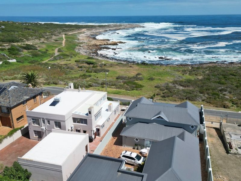 Aerial view of the property showcasing its coastal location, metal roofing, solar water heating, and paved driveway area.