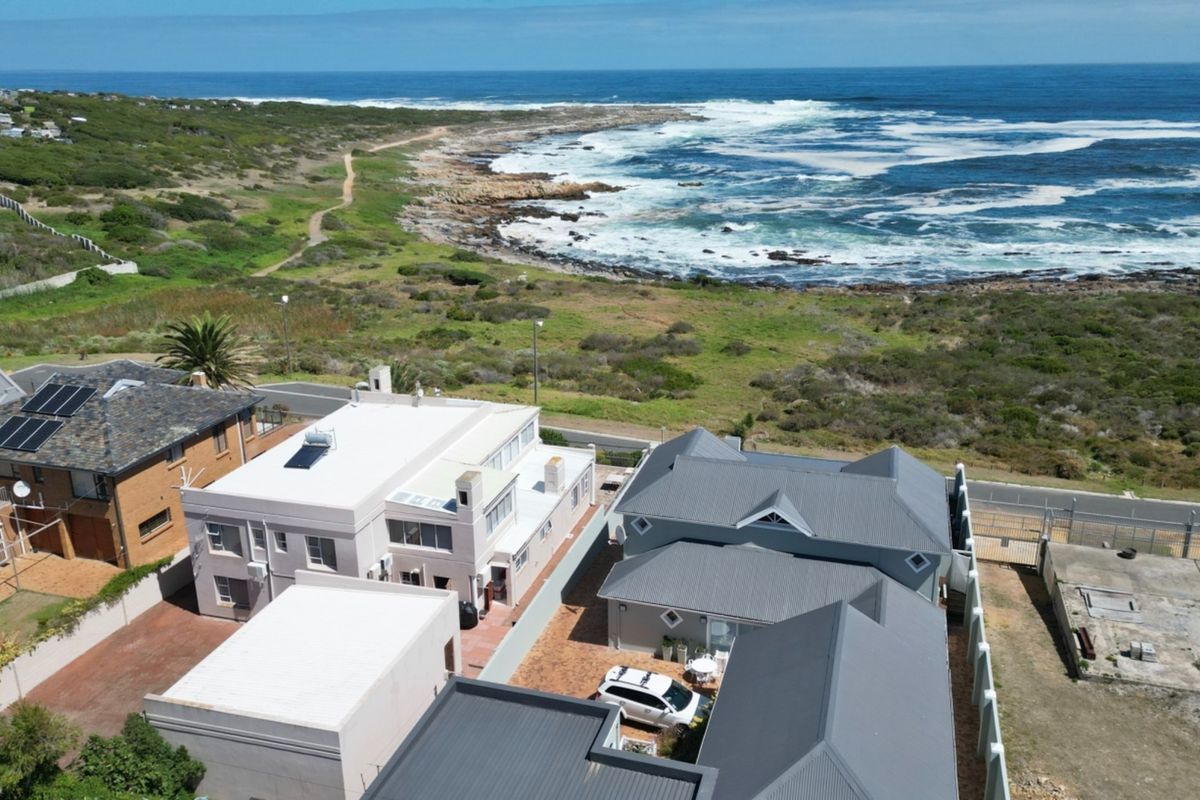 Aerial view of the property showcasing its coastal location, metal roofing, solar water heating, and paved driveway area.