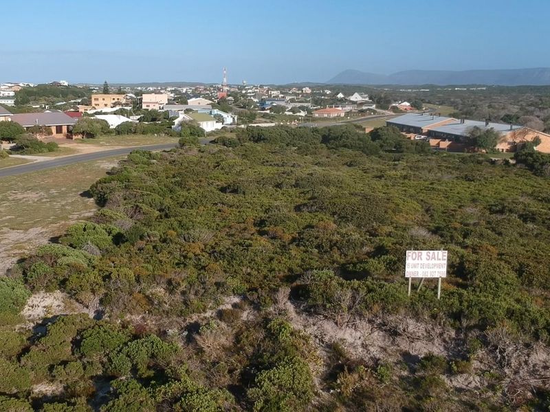 Aerial view of a vacant residential plot featuring native coastal vegetation and a for sale sign, situated in a developed neighbourhood.