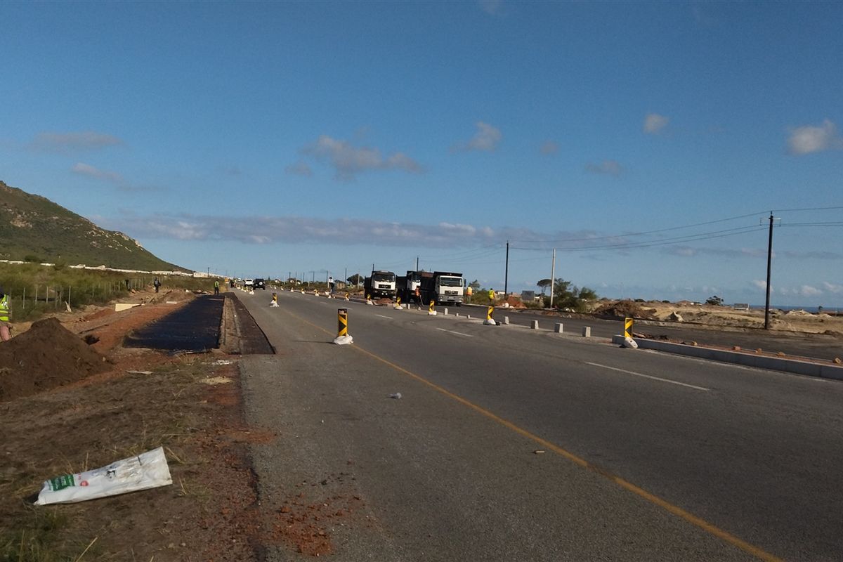 A view of a commercial development site showing road infrastructure, utility poles, and ongoing construction activity along the roadside.