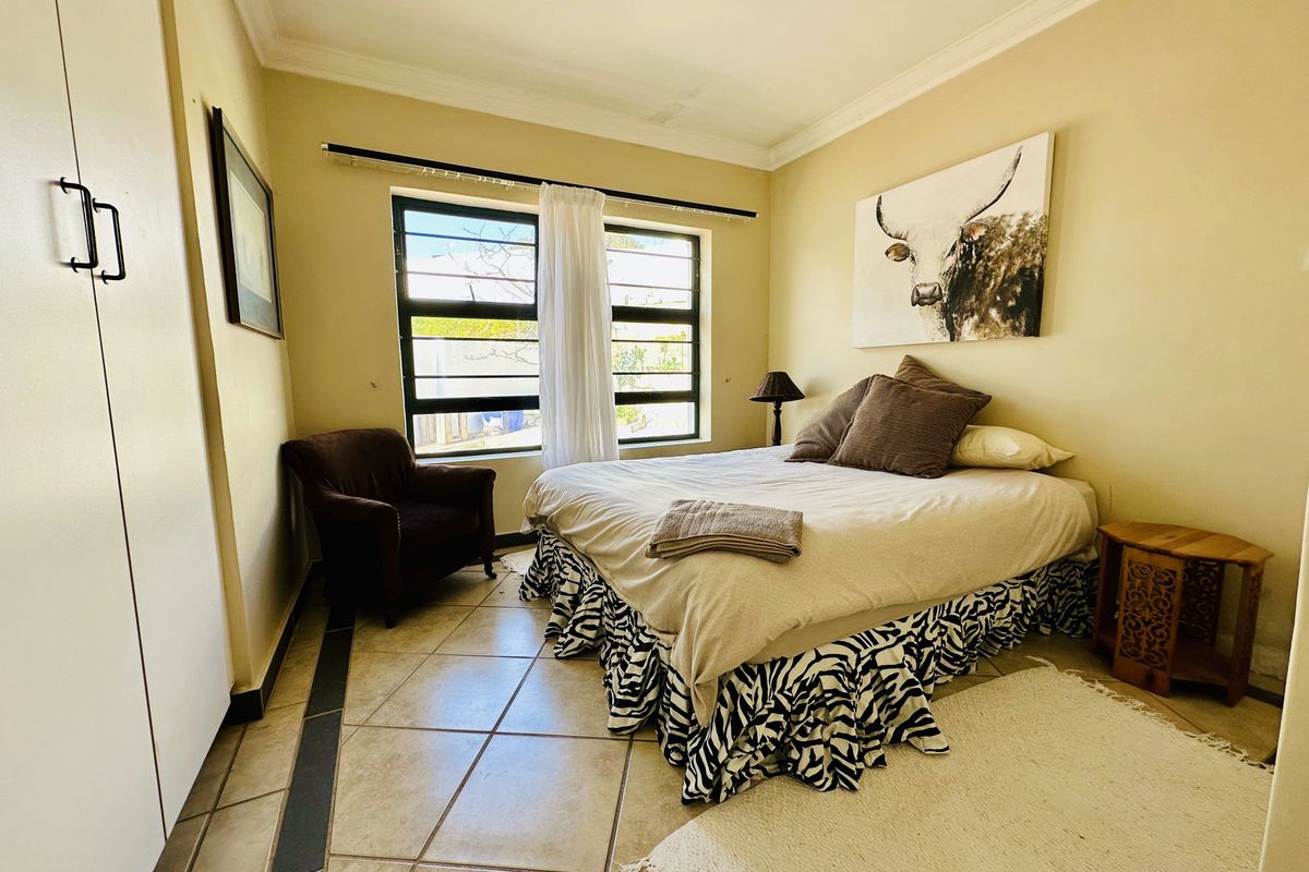 A functional bedroom featuring tiled flooring, a built-in wardrobe, and a window fitted with security bars.