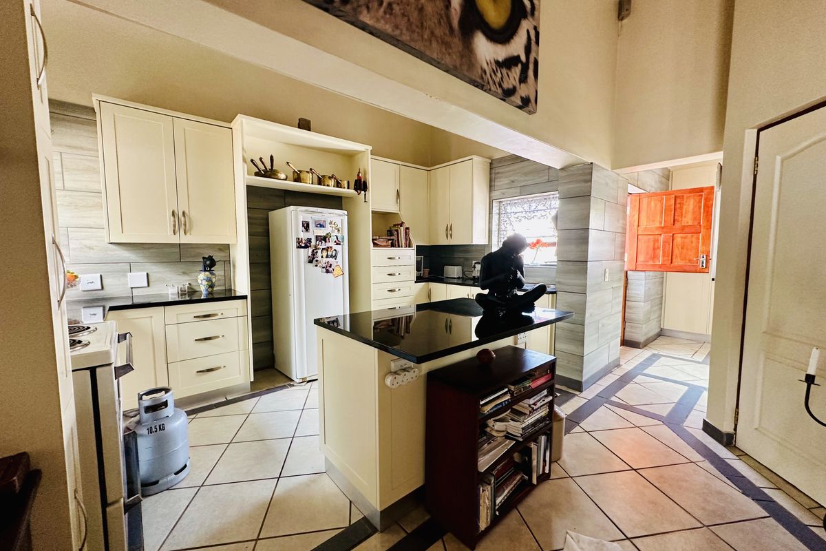 A functional kitchen featuring cream-colored cabinetry, black granite countertops, a central island, and tiled flooring with a neutral backsplash.