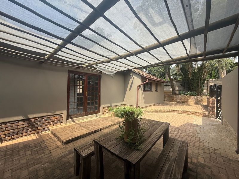 Outdoor patio area featuring brick paving, a shade cloth canopy with timber supports, and direct access to the interior via french doors.