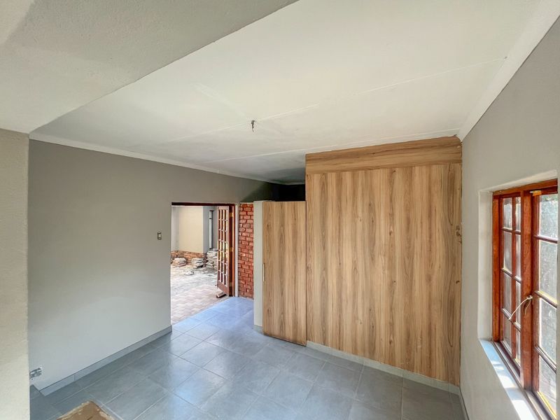 An empty bedroom featuring tiled flooring, built-in wooden cupboards, and a wooden window frame, with access to an outdoor area.