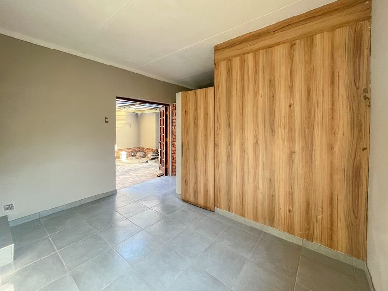An empty bedroom featuring tiled flooring and a large built-in wooden wardrobe, with direct access to an outdoor patio area.