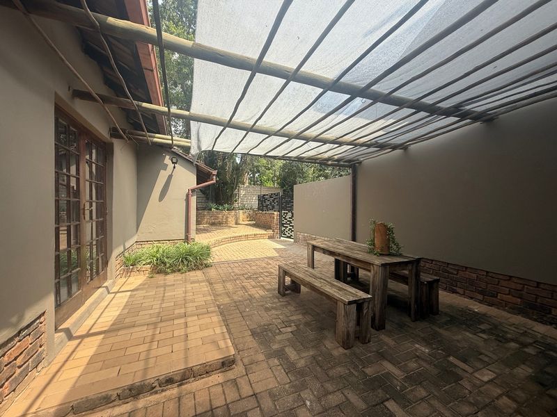 A private outdoor patio area featuring paved flooring, a timber pergola with shade cloth, and direct access to the interior through glass doors.