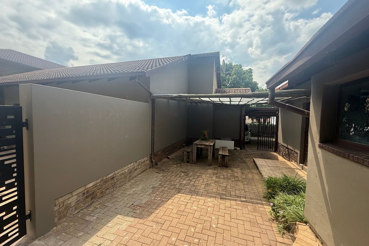 A paved rear courtyard area featuring a pergola structure, boundary walls, and tiled roof sections, providing a functional outdoor space.