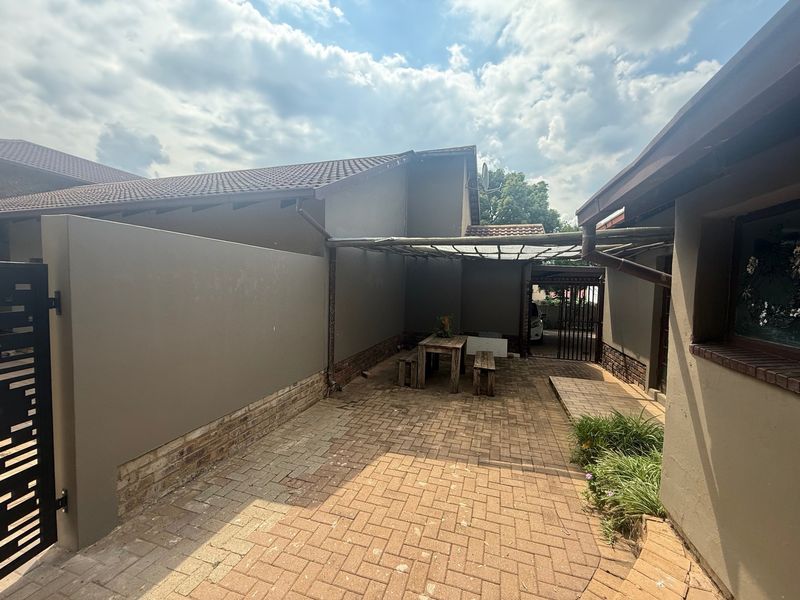A paved rear courtyard area featuring a pergola structure, boundary walls, and tiled roof sections, providing a functional outdoor space.