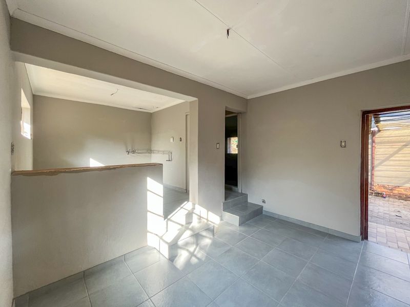 An empty open-plan living area featuring tiled floors, a partial room divider, and direct access to an outdoor patio area.