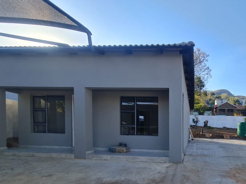 Front exterior view of the apartment featuring a covered patio area, modern grey facade, and aluminium window frames.