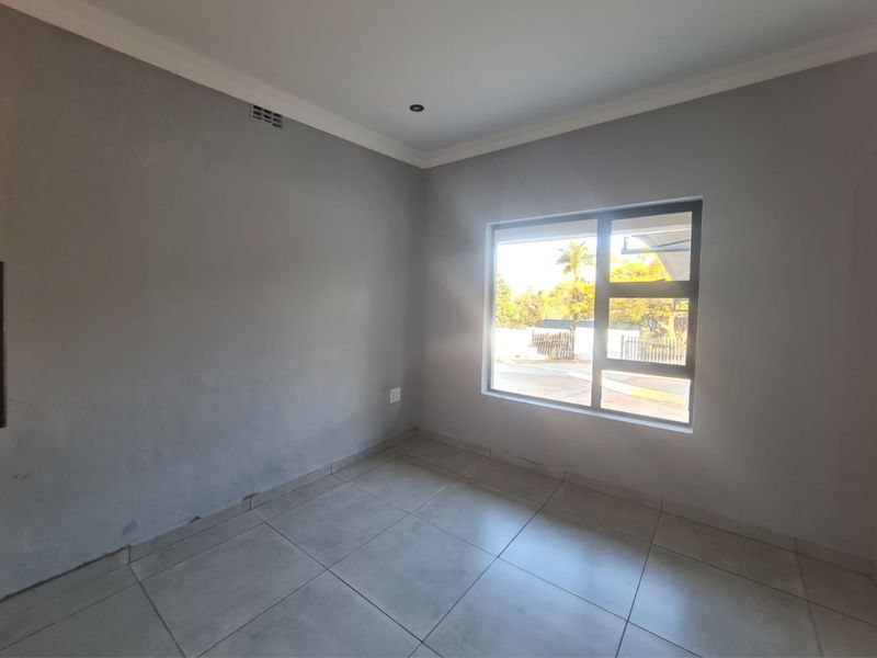 An empty bedroom featuring neutral grey walls, tiled flooring, and a large aluminium-framed window providing natural light.