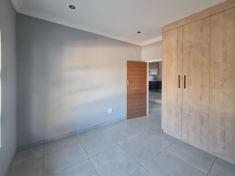 A clean, empty bedroom featuring modern tiled flooring, built-in wooden cupboards, and recessed downlighting, offering a neutral canvas for personalization.