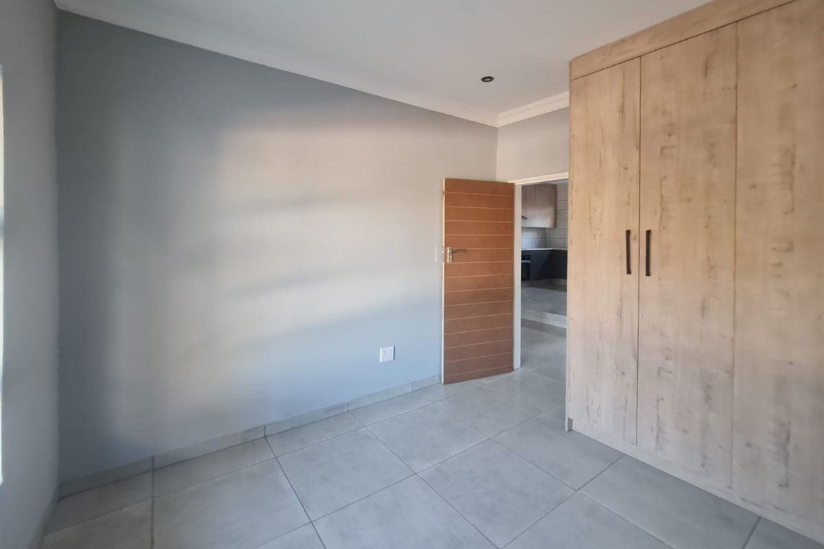 A clean, empty bedroom featuring modern tiled flooring, built-in wooden cupboards, and recessed downlighting, offering a neutral canvas for personalization.