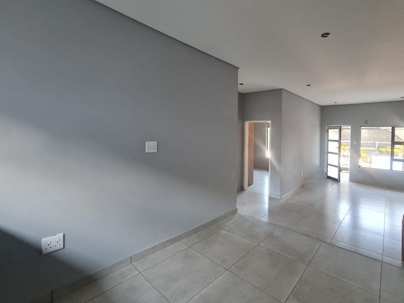 A bright, open-plan living area featuring neutral grey walls, large format floor tiles, and modern aluminium-framed windows and doors.
