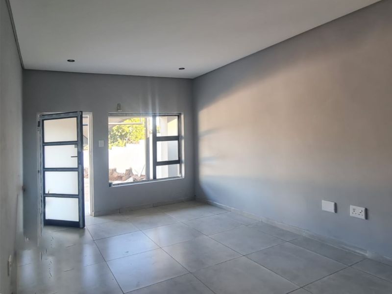 A bright, empty living area featuring neutral grey walls, large aluminium windows, and modern tiled flooring, ready for personalization.