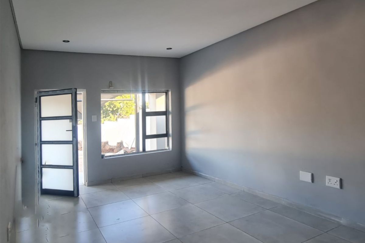 A bright, empty living area featuring neutral grey walls, large aluminium windows, and modern tiled flooring, ready for personalization.