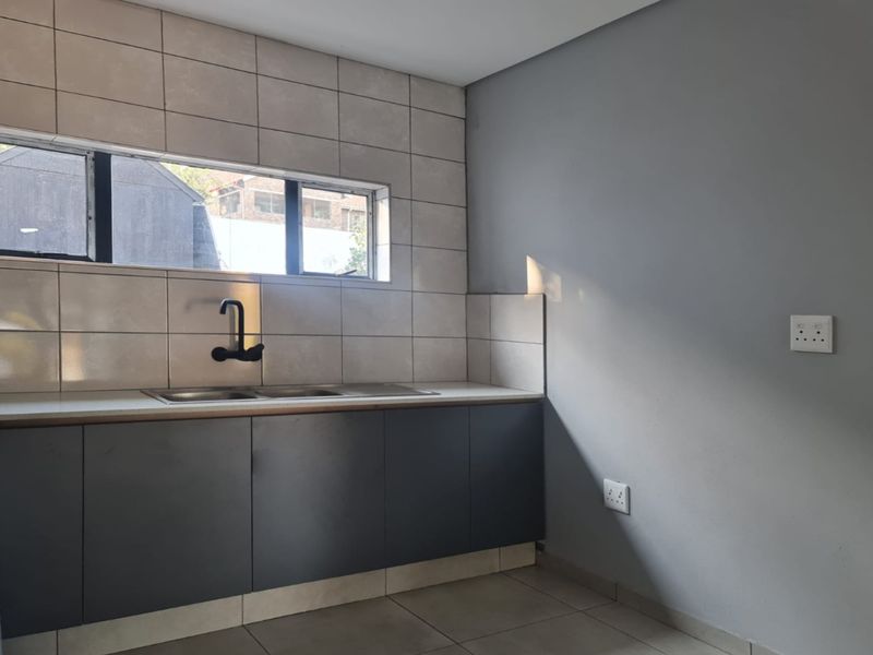 A clean, modern kitchen area featuring dark grey cabinetry, a stainless steel sink with a black mixer tap, and neutral tiled splashbacks.