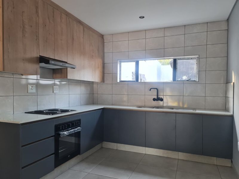 Modern kitchen featuring sleek grey lower cabinetry, wood-tone upper cabinets, stone countertops, integrated oven and hob, and contemporary tiled finishes.