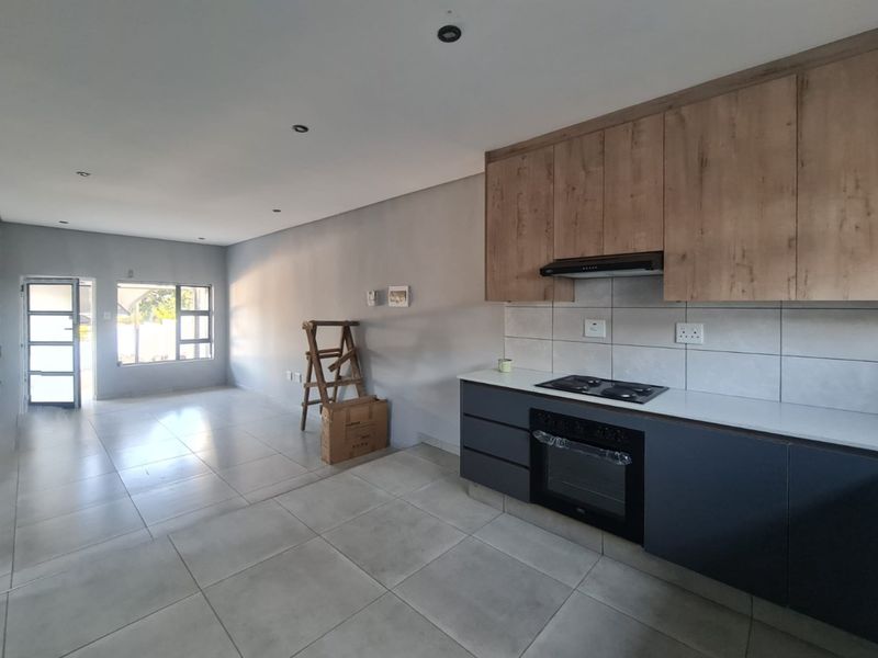 Modern open-plan living area featuring a contemporary kitchen with built-in cabinetry, hob, oven, and extractor fan, complemented by neutral tiled flooring throughout.