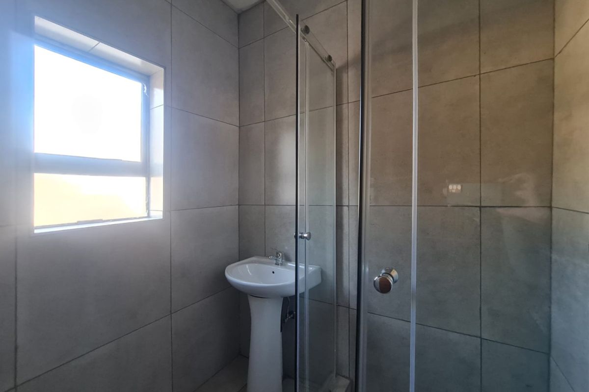 A clean, modern bathroom featuring full-height wall tiling, a pedestal basin, and a glass-enclosed shower unit.