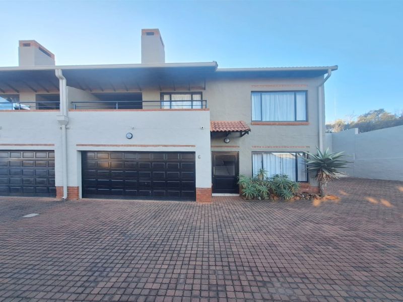 Front elevation of a two-story cluster home featuring a double garage, upper-level balcony, and a paved driveway.