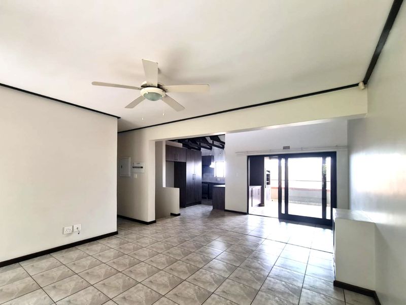 Spacious open-plan living area featuring tiled flooring, a ceiling fan, and seamless flow to the kitchen and outdoor patio through sliding glass doors.