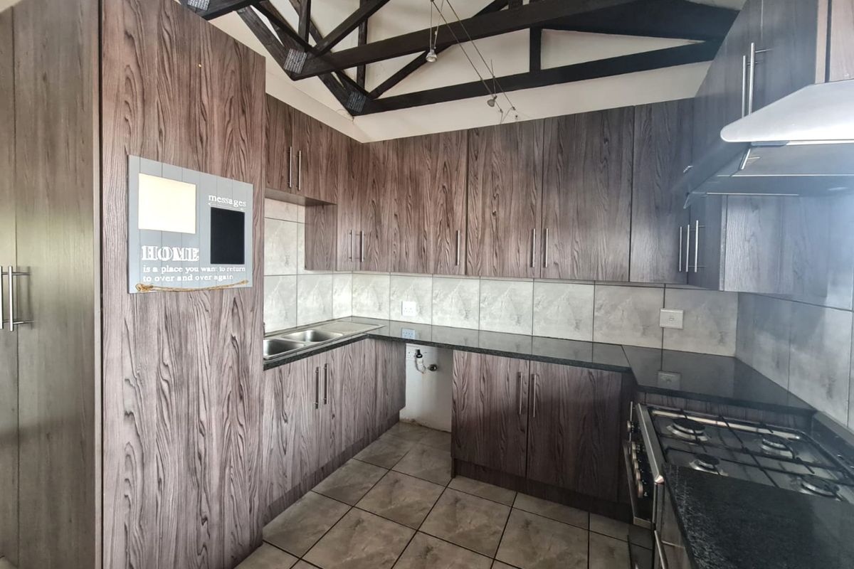 A functional kitchen featuring dark wood-grain cabinetry, granite countertops, a gas hob with extractor, and distinctive exposed timber roof trusses.