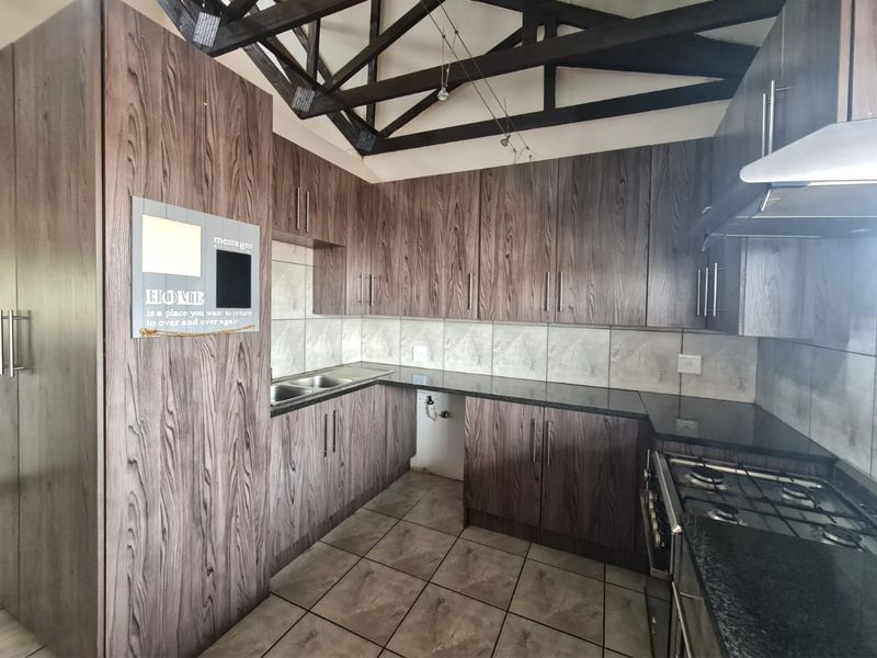 A functional kitchen featuring dark wood-grain cabinetry, granite countertops, a gas hob with extractor, and distinctive exposed timber roof trusses.