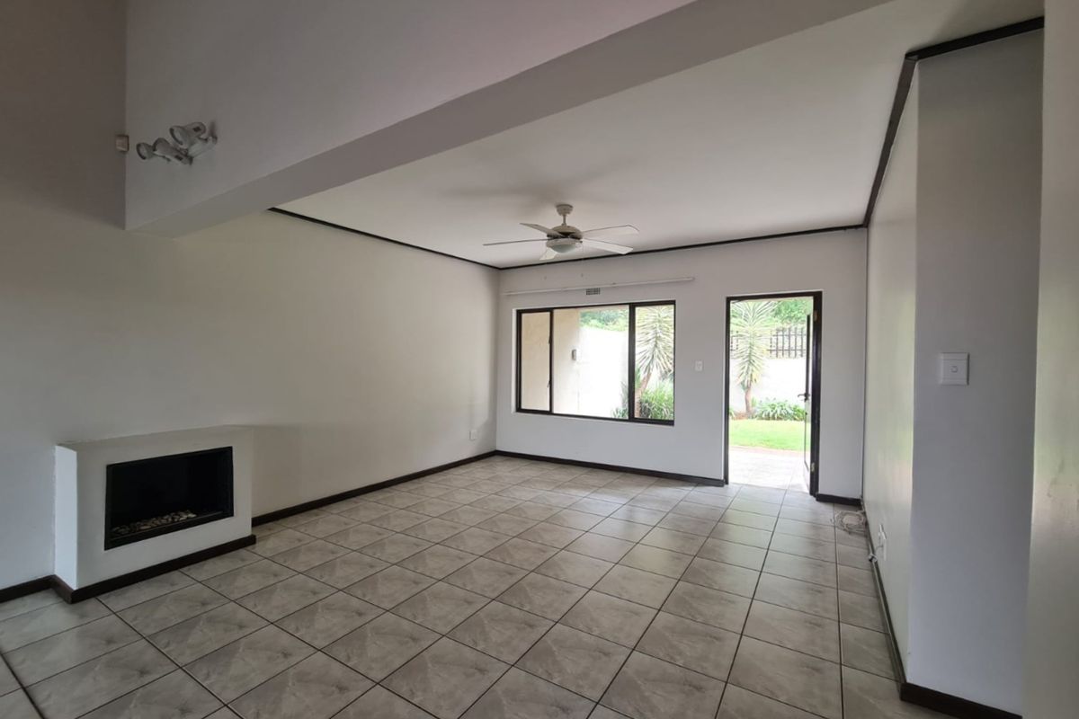 Spacious, light-filled living area featuring tiled flooring, a built-in fireplace, ceiling fan, and direct access to the garden through a glass door.