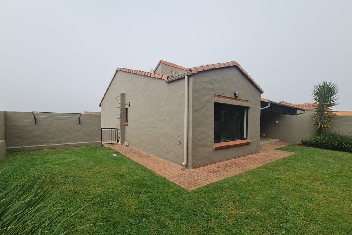 Rear view of the cluster property featuring a private garden, paved walkway, and plastered exterior walls with terracotta roof tiles.