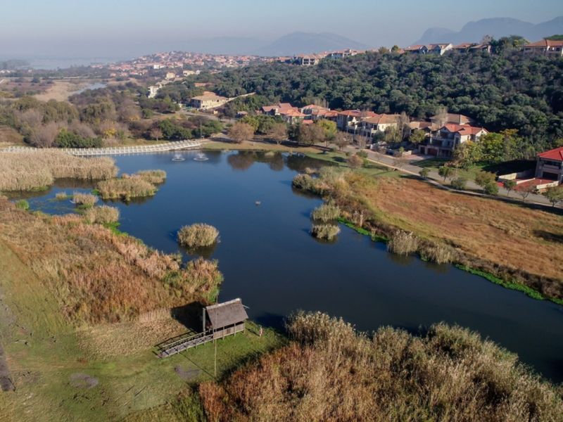 Aerial view of the estate featuring a large lake, landscaped surroundings, a thatched gazebo, and a wooden walkway.
