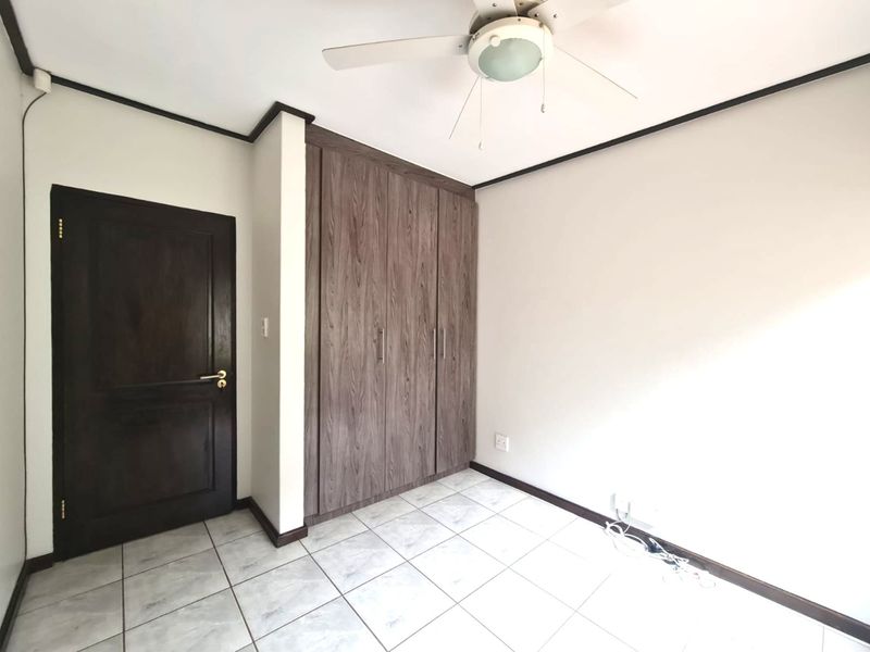 A clean, empty bedroom featuring tiled flooring, a ceiling fan, and built-in wooden cupboards with a matching timber door.