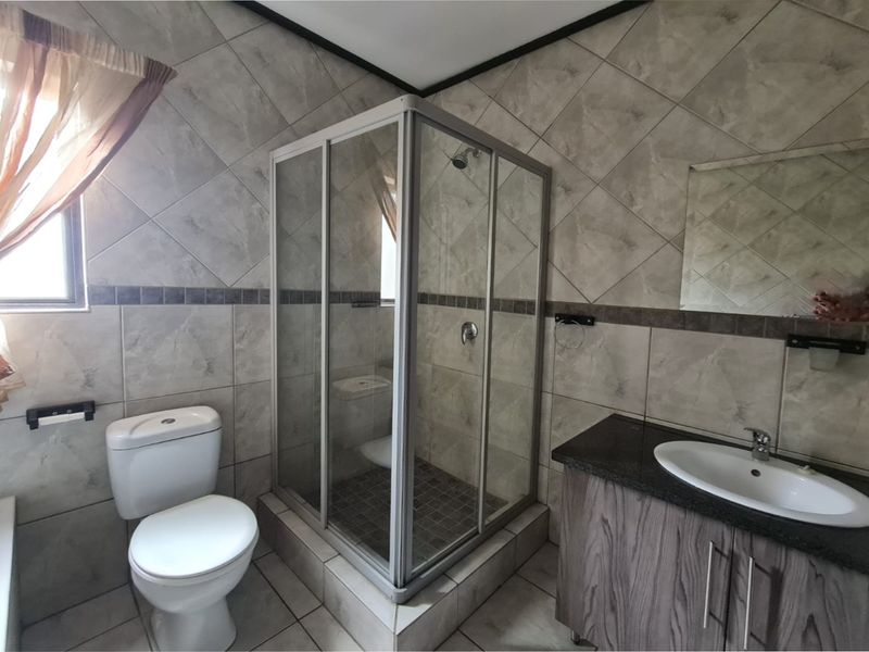 A functional bathroom featuring a corner shower enclosure, a vanity unit with a basin, and neutral wall and floor tiling.