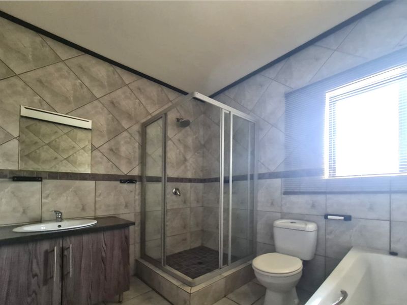A functional bathroom featuring a shower enclosure, bathtub, vanity with basin, and tiled finishes throughout.
