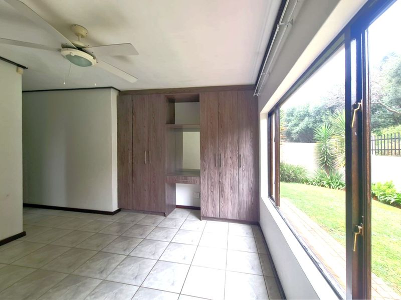 Spacious bedroom featuring built-in wooden cupboards, tiled flooring, a ceiling fan, and large sliding doors providing direct access to the garden.