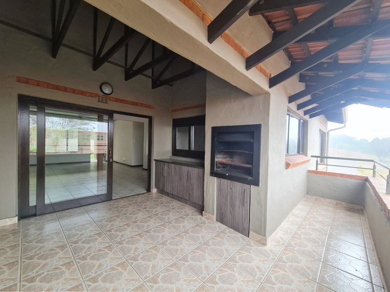 Covered patio featuring a built-in braai, tiled flooring, and exposed timber roof trusses, providing a functional outdoor entertainment space.