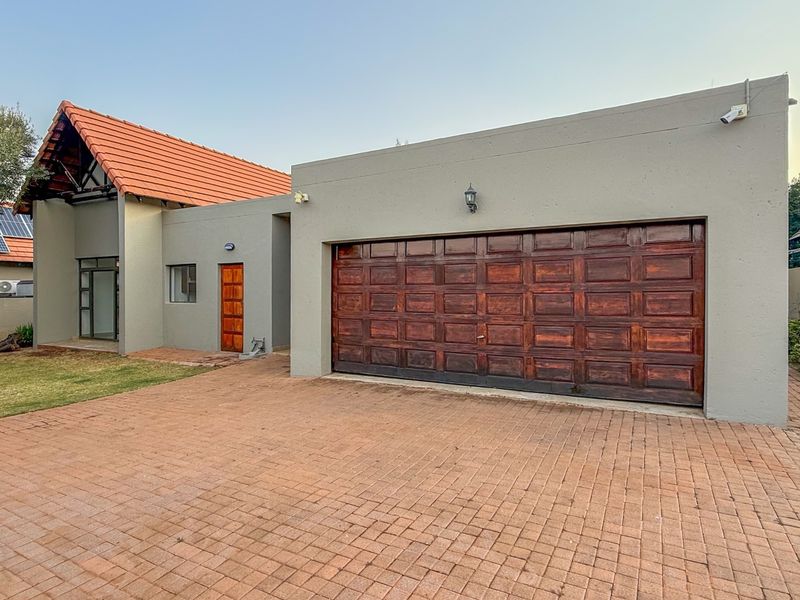 Front view of the property featuring a paved driveway, a double garage with a wooden door, and a tiled roof structure.