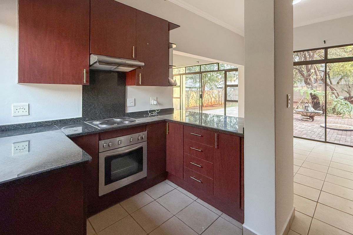 A functional kitchen featuring dark wood cabinetry, granite countertops, built-in oven and hob, with direct access to an outdoor patio area.