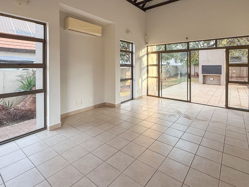 Spacious, light-filled living area featuring neutral tiled flooring, exposed ceiling beams, and large sliding glass doors providing direct access to the outdoor patio.
