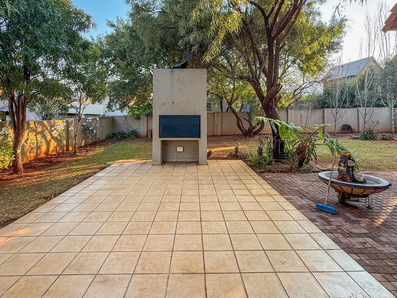 A spacious outdoor patio area featuring a built-in braai, tiled flooring, and direct access to the surrounding garden and boundary wall.