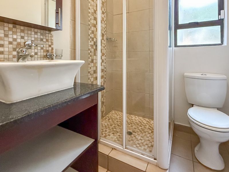A functional bathroom featuring a vessel sink on a granite vanity, a glass-enclosed shower with mosaic accents, and a standard toilet.