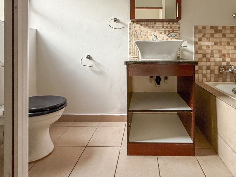 A functional bathroom featuring a vessel sink vanity, built-in bathtub with mosaic tile surround, and standard toilet facilities.